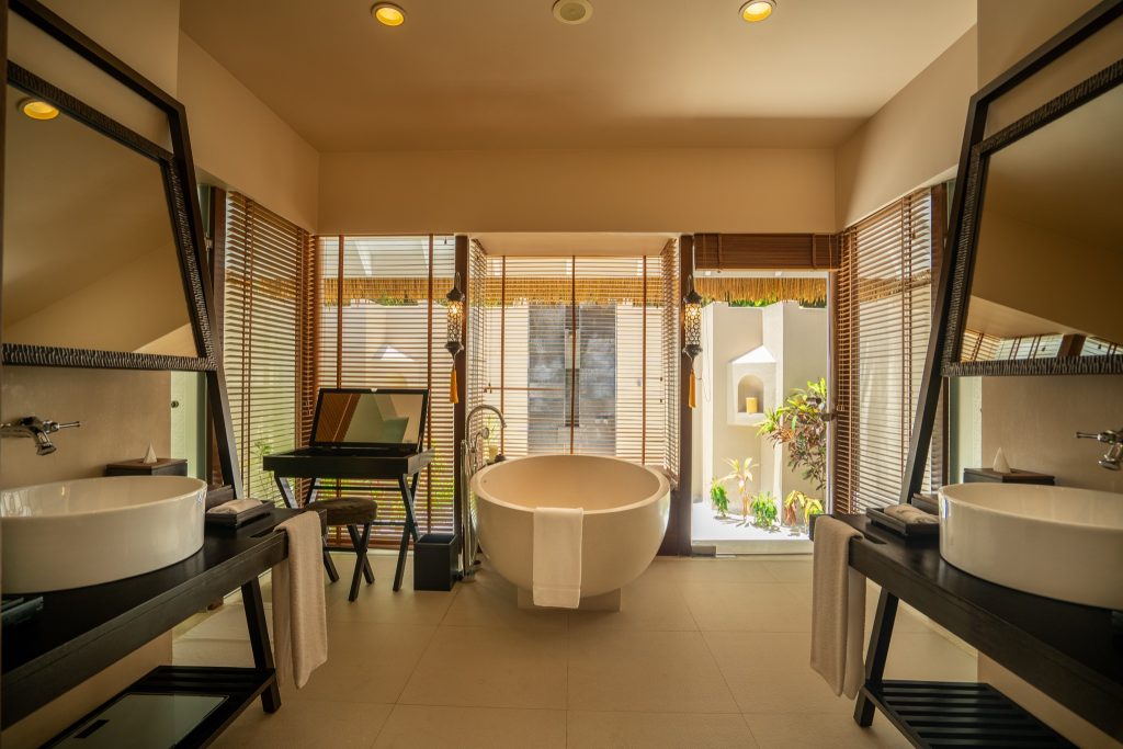 Badezimmer der Beach Family Suite im Ayada Maldives mit freistehender Badewanne, Holzjalousien und Tageslicht