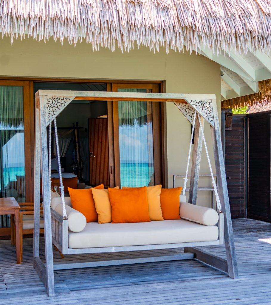 Terrasse der Sunset Lagoon Suite im Ayada Maldives mit Holzschaukel, orangefarbenen Kissen und Blick auf das Meer