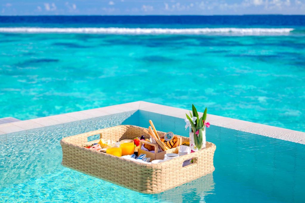 Geflochtener Frühstückskorb mit Orangensaft, Backwaren und Schälchen auf dem Poolwasser im Baglioni Resort Maldives