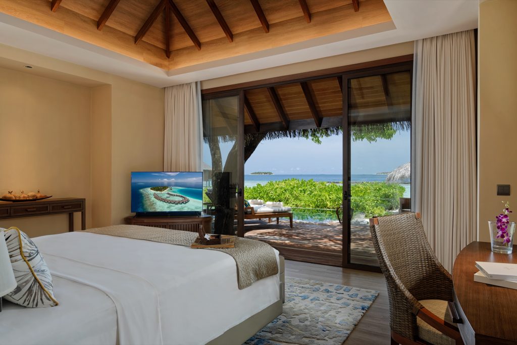 Hotelzimmer mit großem Bett, Holzboden, Schreibtisch, Rattan-Stuhl und direktem Blick auf Terrasse und Ozean