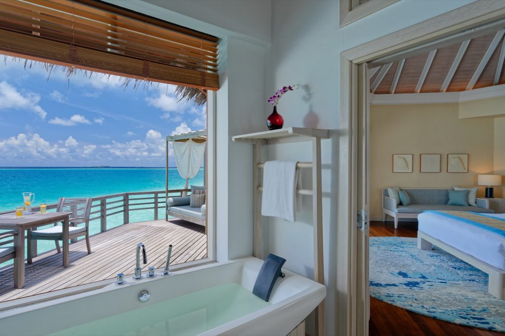 Hotelzimmer mit Meerblick, weißer Badewanne, Holzdielen, Terrasse mit Sitzgelegenheiten und großem Bett Malediven