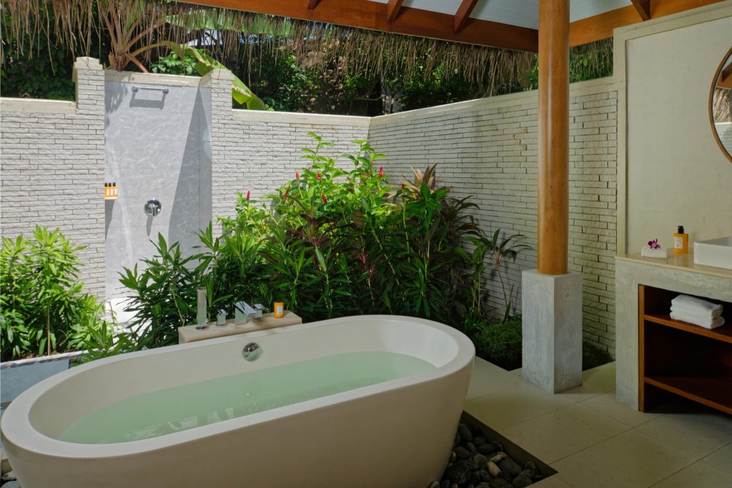 Freiluft-Badezimmer mit freistehender Badewanne, Dusche, grauen Steinwänden und beige-braunem Fliesenboden