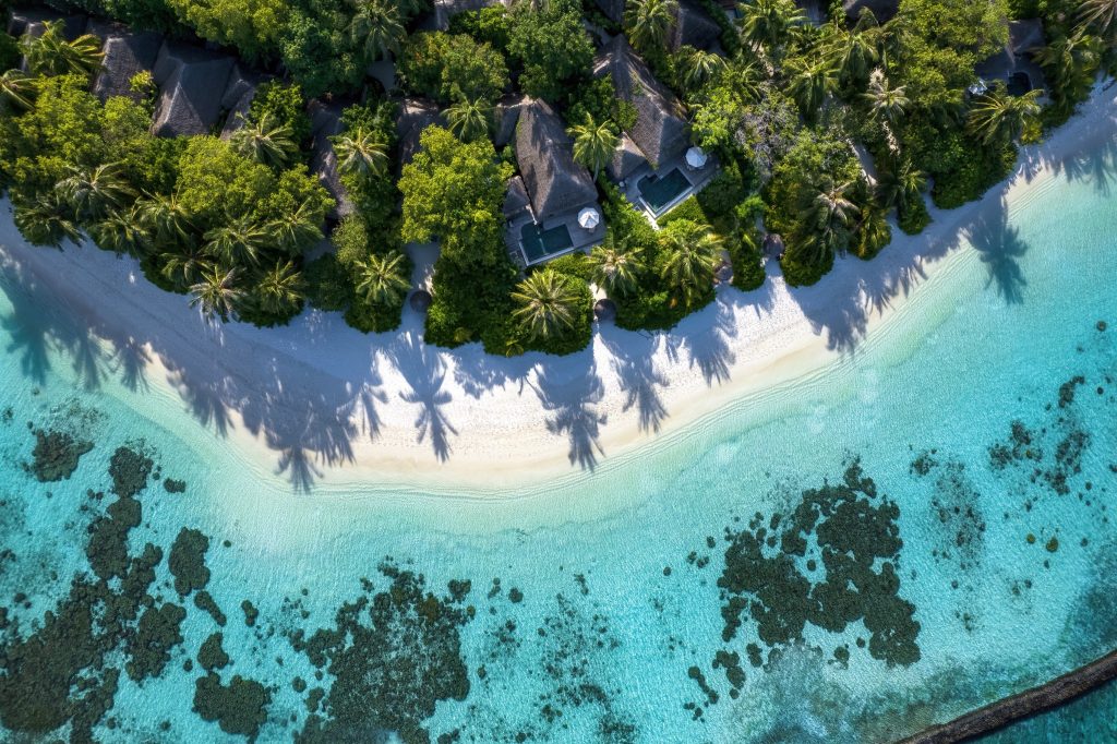 Vogelperspektive auf Baros Maldives Strand mit türkisfarbenem Wasser, weißen Sandstrand und grasgedeckten Bungalows