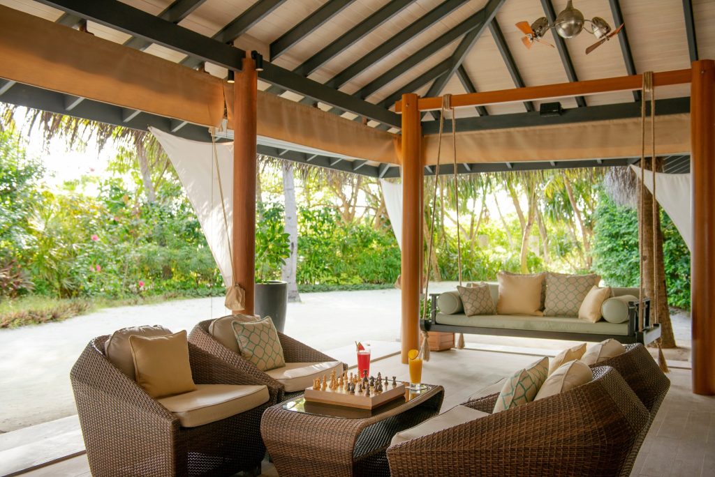 Überdachte Terrasse der Sails Bar mit Rattan-Sesseln, Glastisch, Schachbrett und bunter Getränke auf den