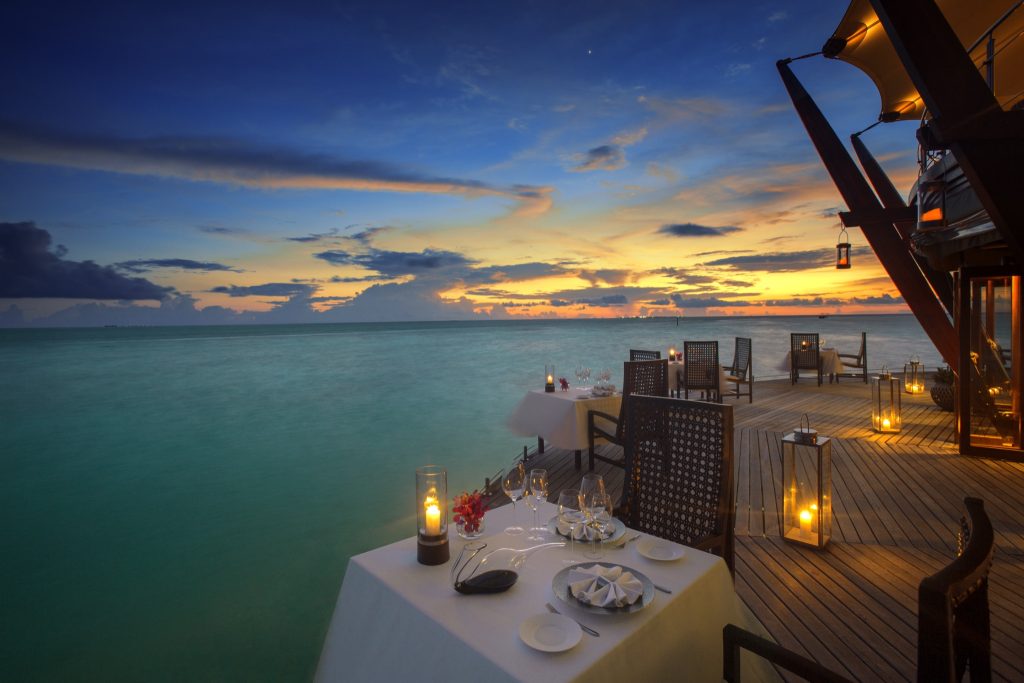 Außenterrasse des Restaurant Lighthouse in Baros Maldives mit weißen Tischdecken, Holzdielen und Sonnenuntergang
