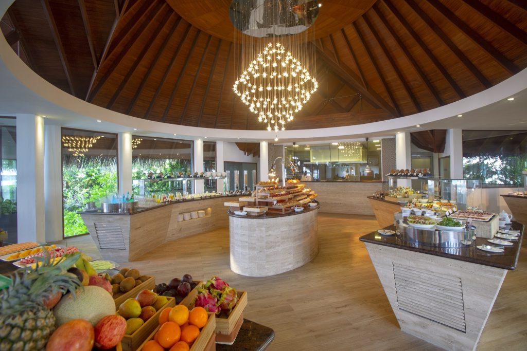 Rundes Buffet im Restaurant Lime von Baros Maldives mit hellem Stein, Holz-Dach und großen Fenstern