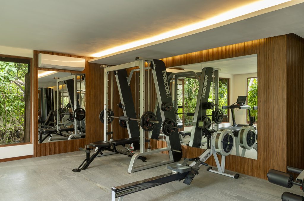 Fitnessraum im Baros Maldives mit Hantelbank, Smith-Maschine, Rudergerät, großen Spiegeln und Fensterblick auf grüne.
