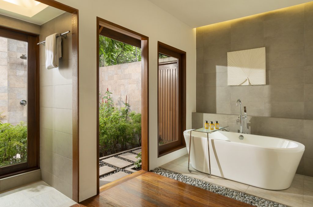Modernes Badezimmer in Baros Maldives mit freistehender weißer Badewanne, grauen Kieselsteinen und Fenster zum Garten