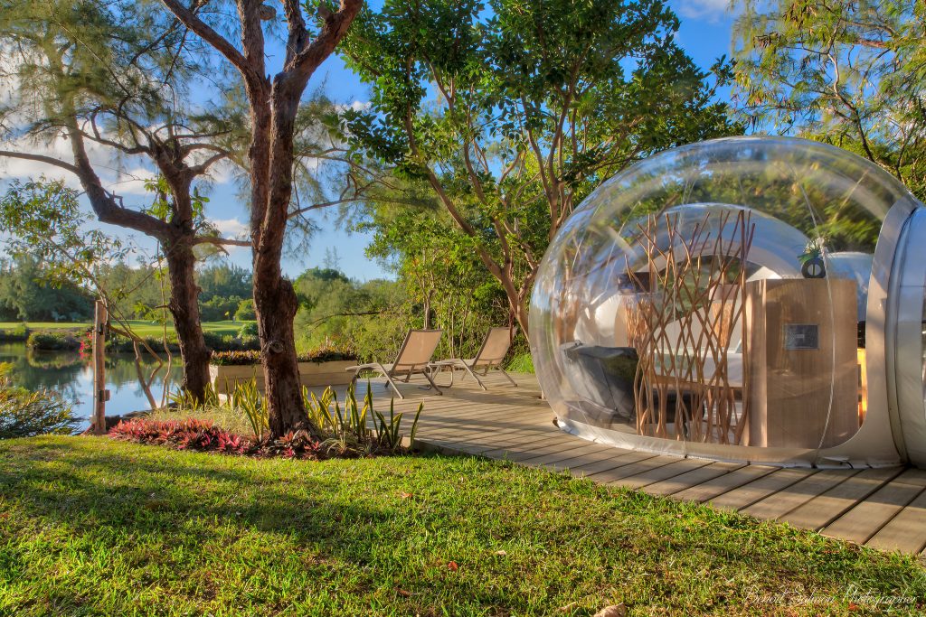 Transparente Bubble Lodge auf Holzplattform mit modernem Interieur, Liegestühlen und Vegetation am Wasser in Mauritius