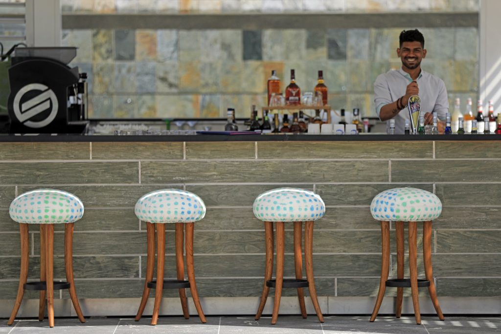 Moderne Hotelbar im Beach Bistro des C Mauritius mit Holzpaneelen, vier Barhockern und Getränken auf der Theke