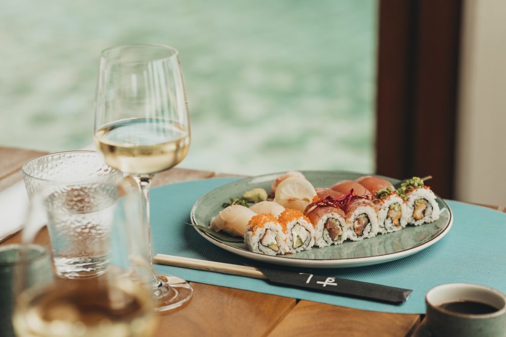 Liebevoll gedeckter Tisch im Restaurant Wok and Roll mit Sushi- und Sashimi-Rollen, Weißweinglas und Wasserglas