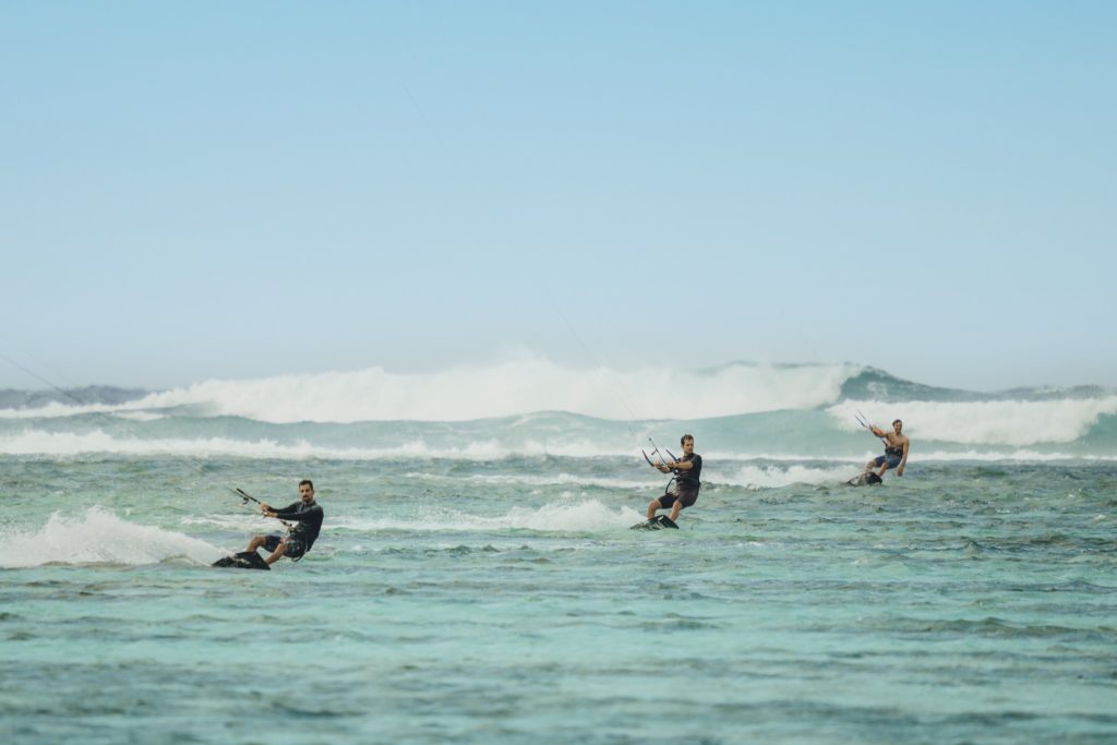 Drei Personen kitesurfen auf dem Meer mit blauem Himmel und weißen Wellenkronen im Tageslicht