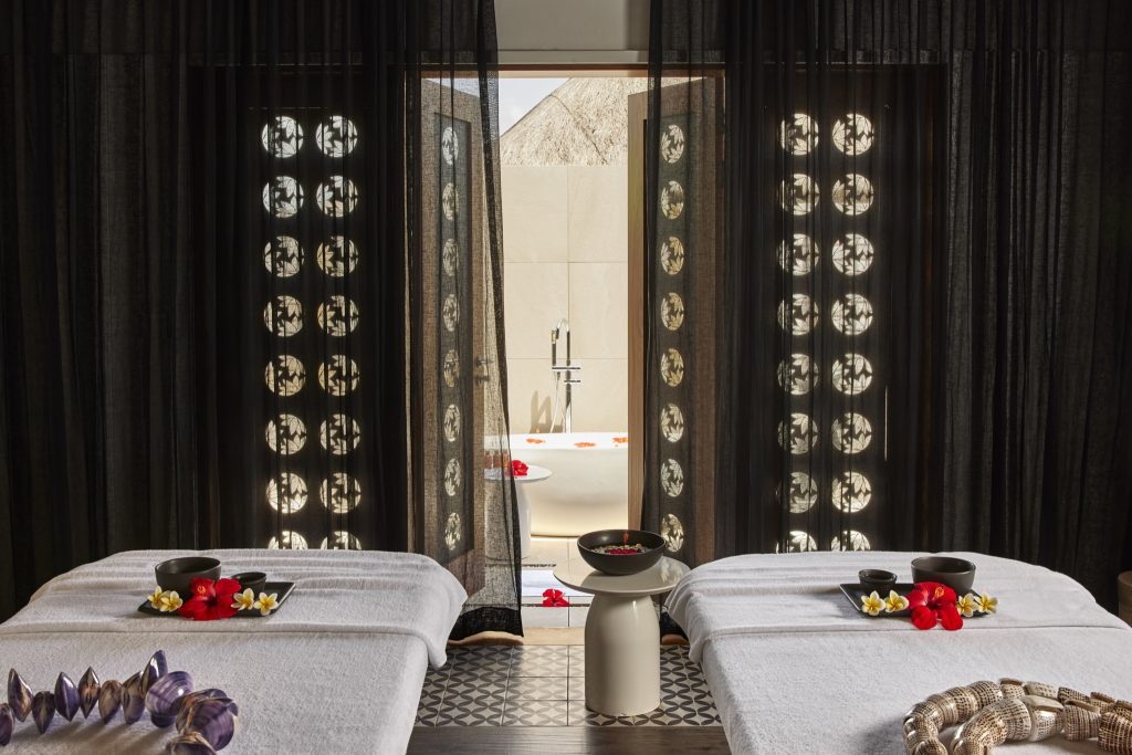 Spa-Bereich mit zwei Massageliegen, gemusterter Bodenfliese, dunklen Vorhängen und freistehender Badewanne