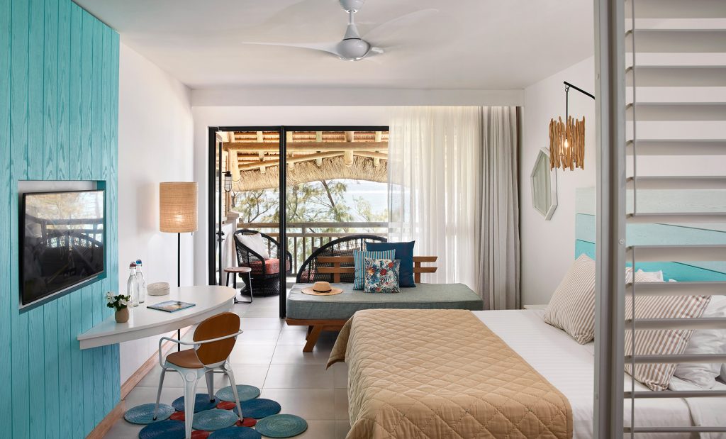 Deluxe Room im C Mauritius mit großem Bett, türkisfarbener Holzwand, Schreibtisch und Balkon mit Meerblick