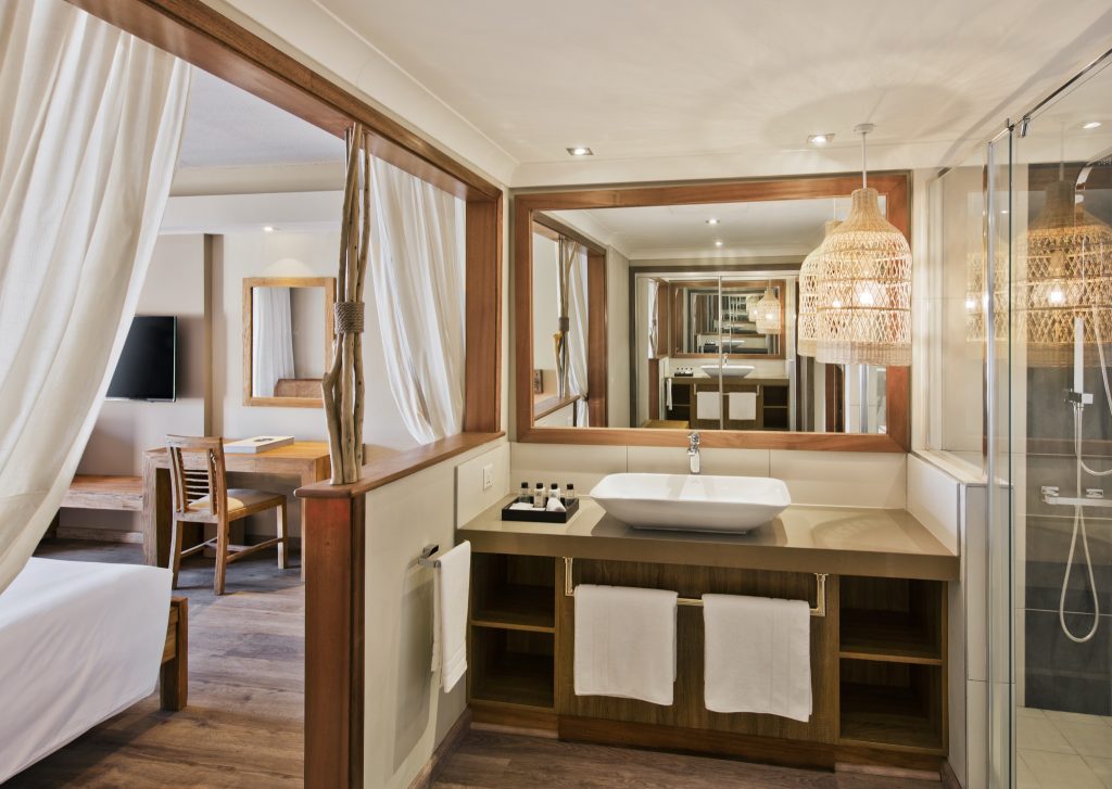 Modernes Prestige Room Hotelzimmer mit offenem Badezimmer, Holzdetails, großem Spiegel und hellem Stoffvorhang