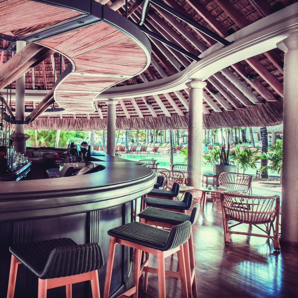 Offene Hotelbar mit rundem Palmdach, dunklem Holz, Rattan-Barhockern und Holzboden neben Pool