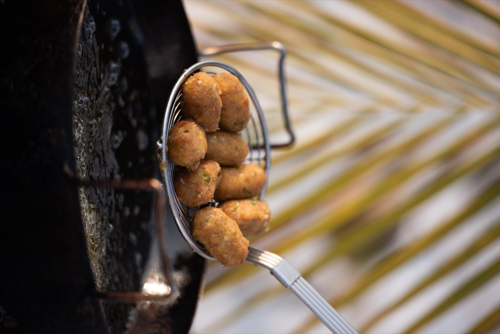 Nahaufnahme von frittierten Teigbällchen in einem silbernen Sieb über einer schwarzen Pfanne mit glitzerndem Öl in der Küche