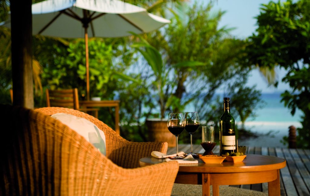Terrasse der Conch Bar im Coco Palm Dhuni Kolhu mit Holztisch, Weinflasche, Rattansessel, Sonnenschirm und Meerblick