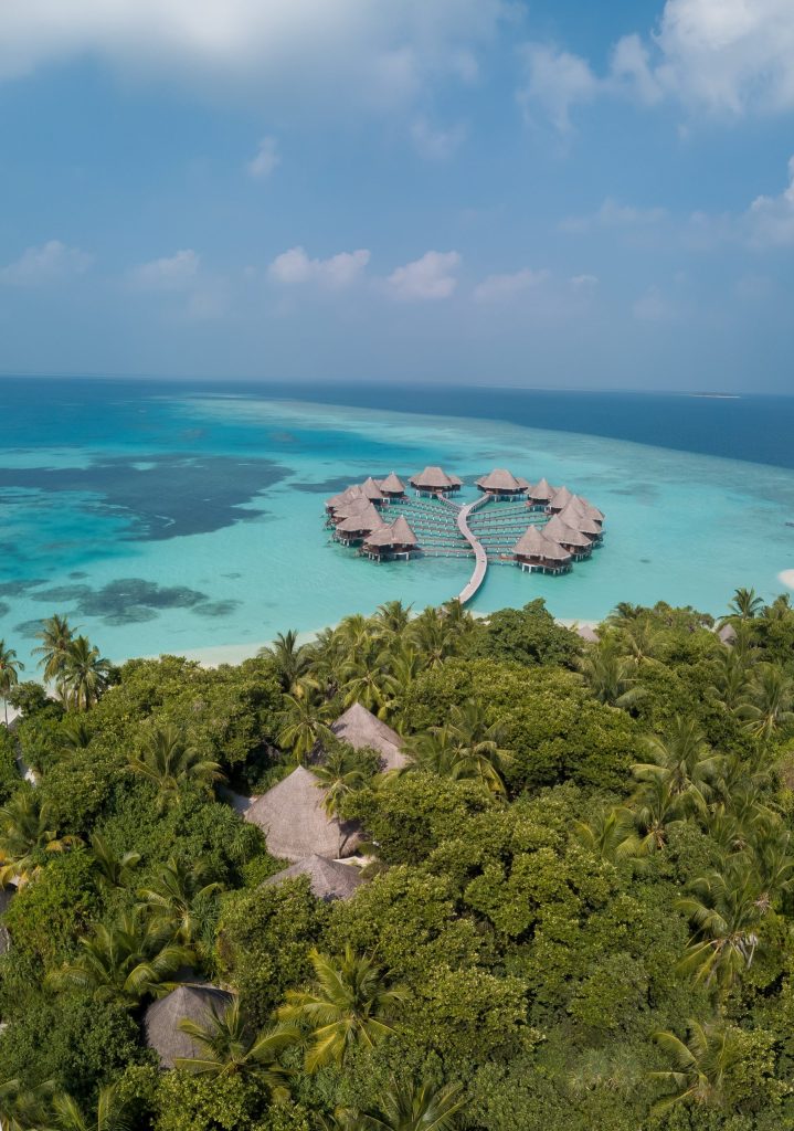 Resort auf Stelzen mit Reetdächern über türkisfarbenem Wasser, verbunden durch Holzstege, umgeben von grüner Vegetation