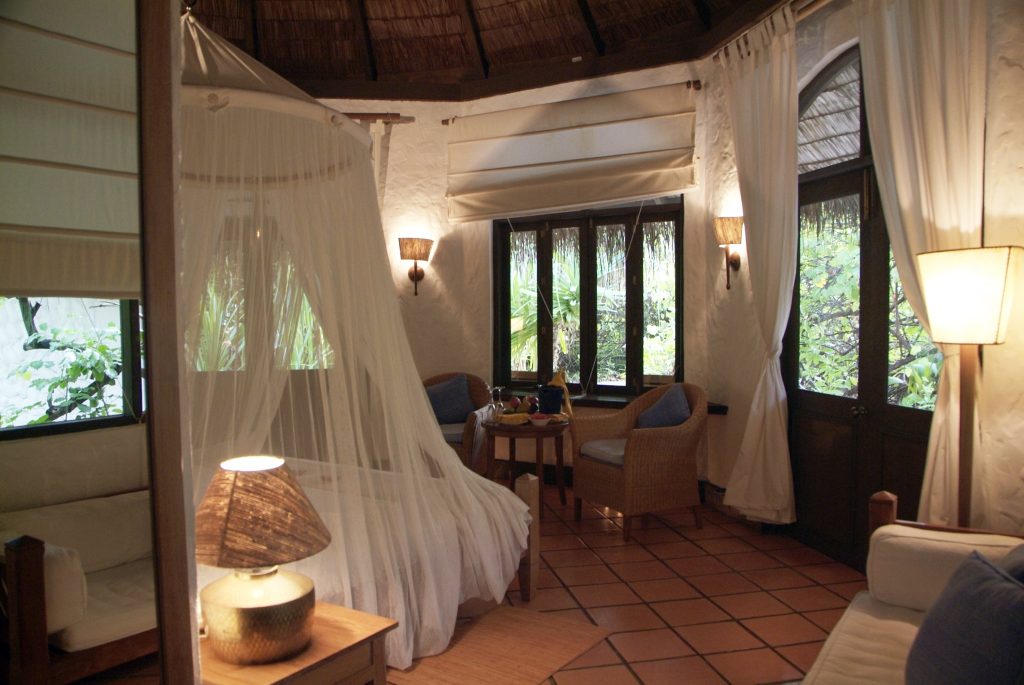 Gemütliches Zimmer der Beach Villa mit Moskitonetz, Rattanmöbeln und großen Holzfenstern zur grünen Landschaft
