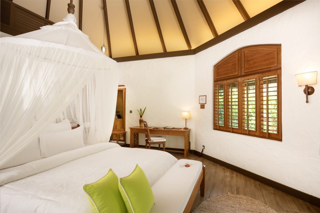 Deluxe Pool Villa Zimmer im Coco Palm Dhuni Kolhu mit weißem Baldachinbett, Holzboden und Tageslichtfenster