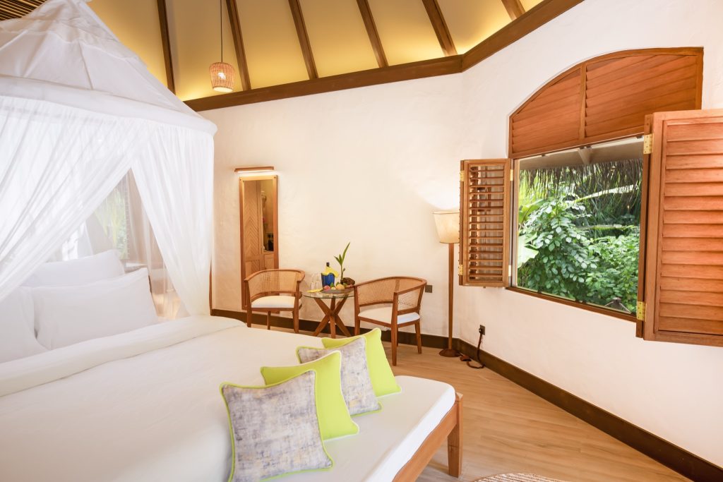 Deluxe Pool Villa Zimmer mit weißem Baldachinbett, hellem Holz, grün akzentuierten Kissen und Fenster mit Blick