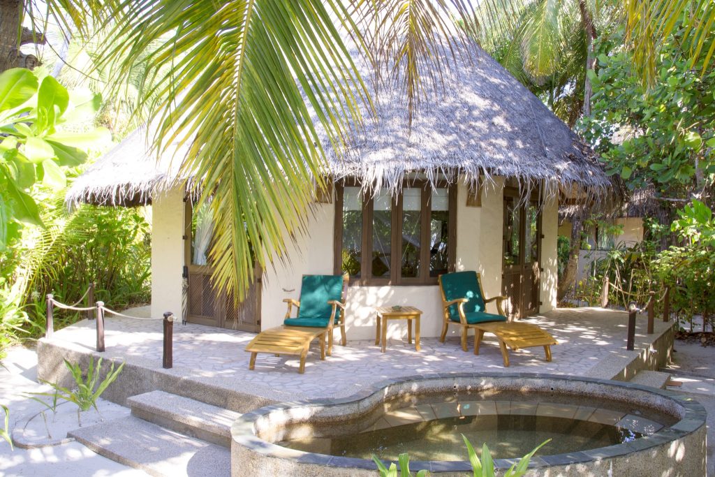 Kleines Hotelbungalow mit Strohdach, Terrasse mit grünen Holzliegen und kleinem Pool