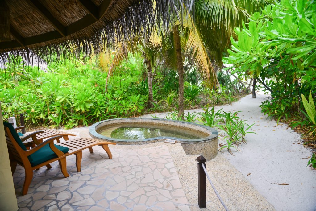 Terrasse der Deluxe Villa mit zwei Holz-Liegestühlen, kleinem Steinpool und tropischen Pflanzen auf den