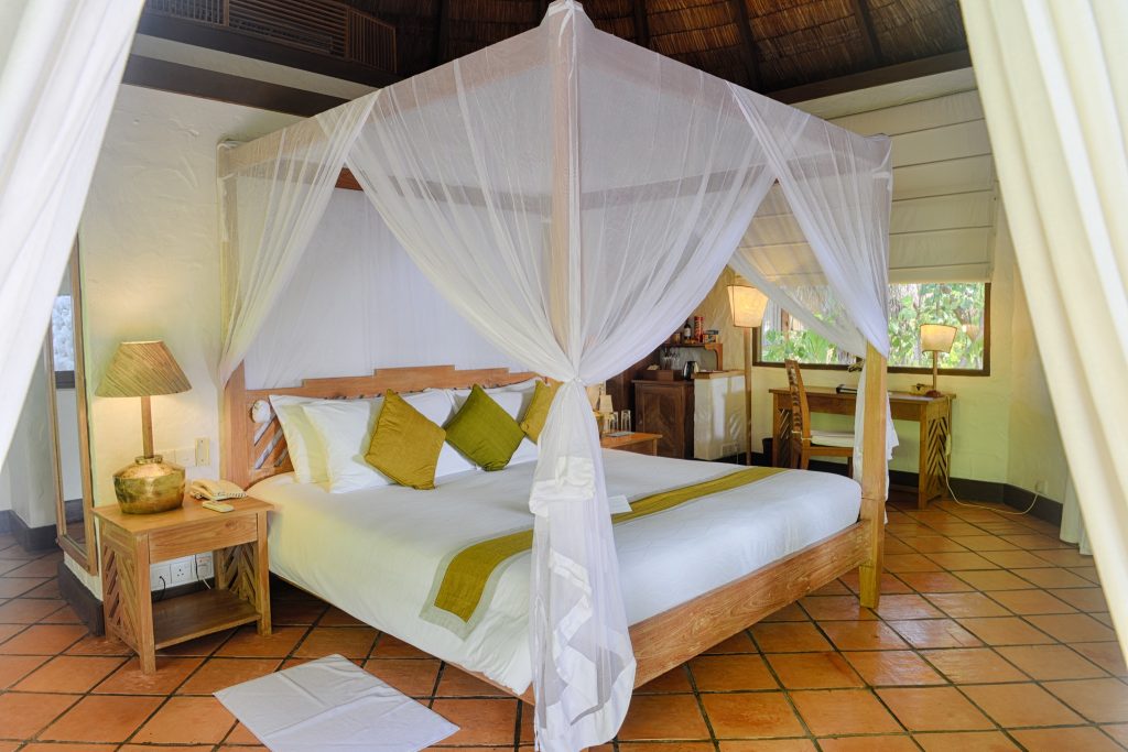 Zimmer der deluxe villa im Coco Palm Dhuni Kolhu mit Himmelbett, Holzmöbeln, Terrakottafliesen und Tageslicht
