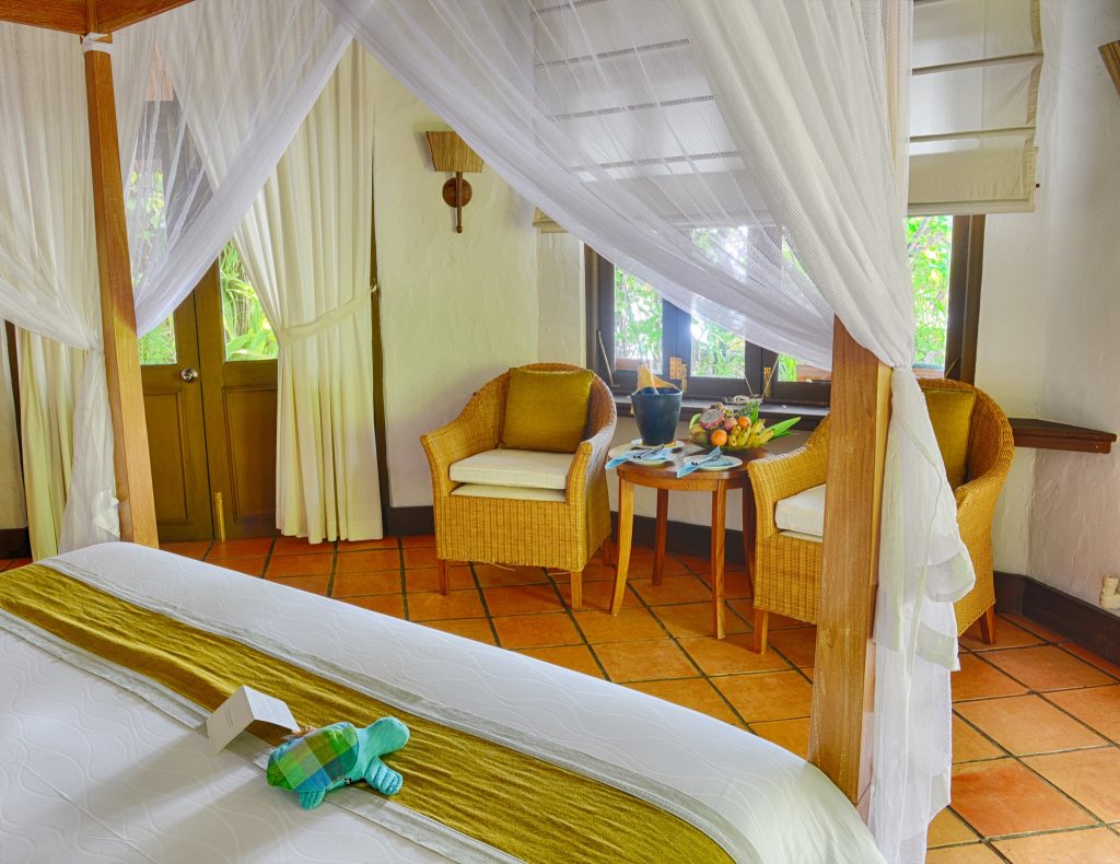 Deluxe Villa Zimmer mit Holz-Himmelbett, weißen Vorhängen, Terrakottafliesen, Korbsesseln und Holztisch