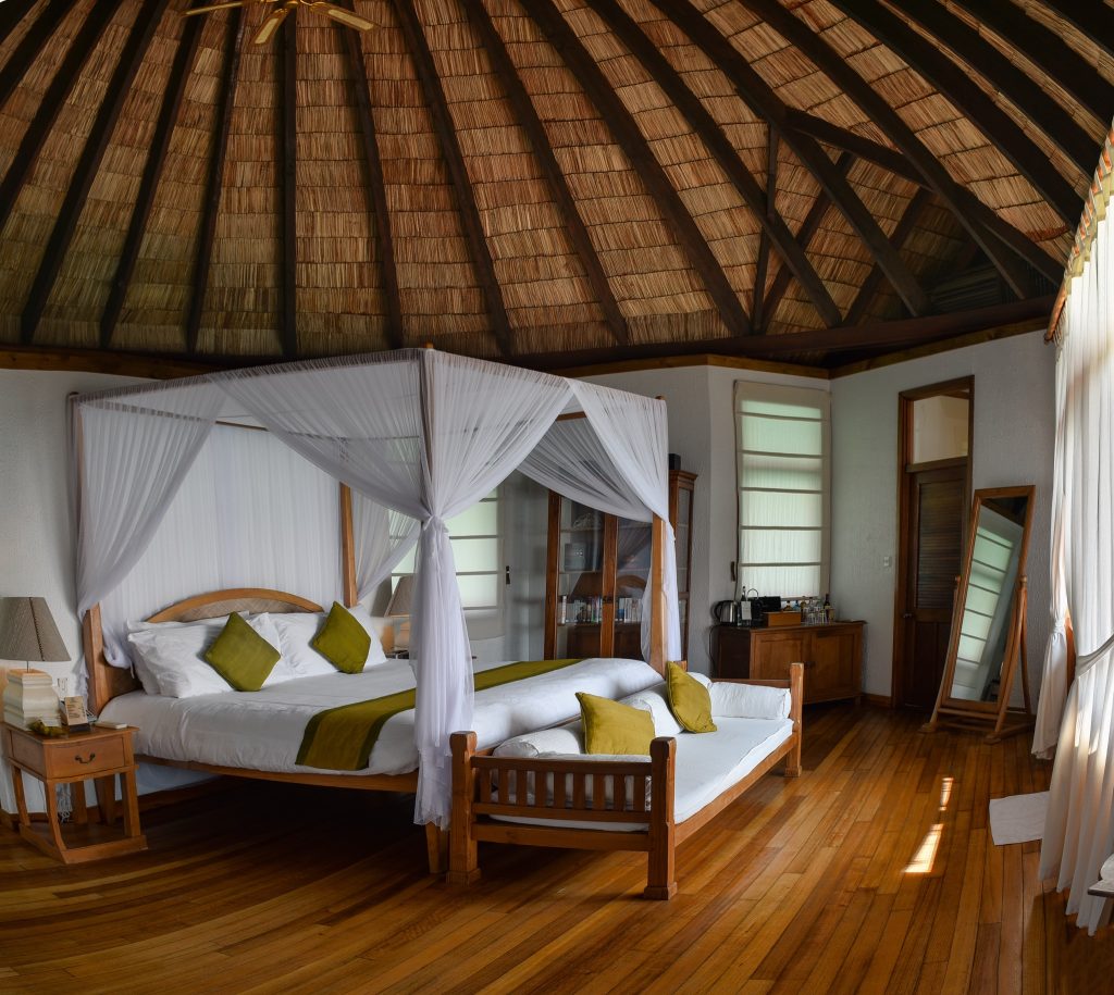 Geräumiges Zimmer der Lagoon Villa im Coco Palm Dhuni Kolhu mit Himmelbett, Holzwänden und großen Fenstern