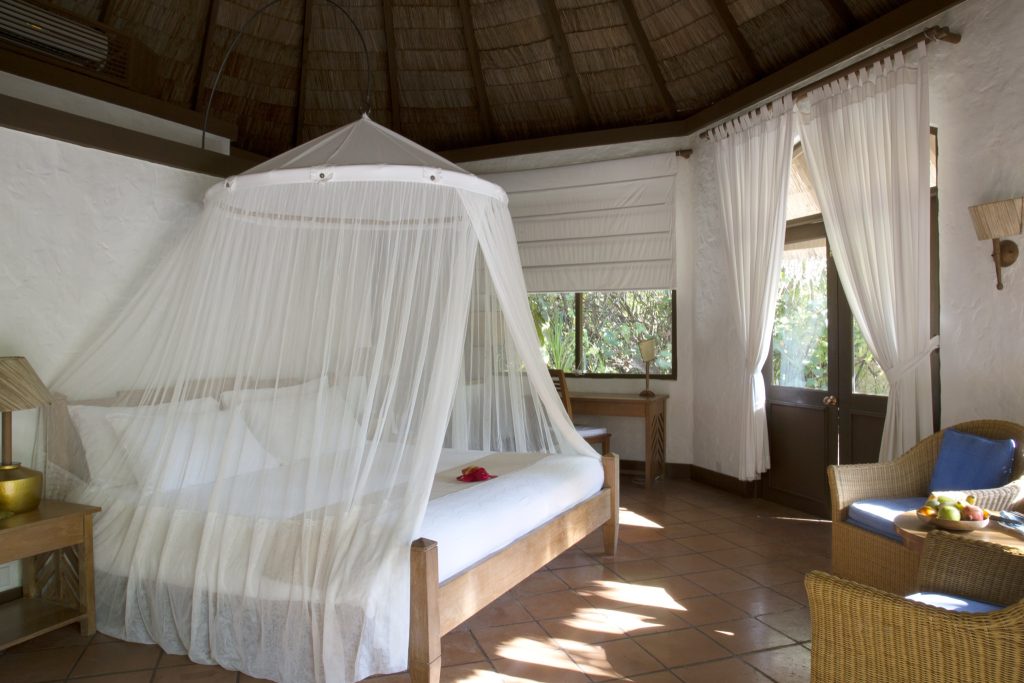 Zimmer der Sunset Beach Villa mit großem Bett, weißem Moskitonetz, hellen Holz- und Rattanmöbeln und großen Fenstern