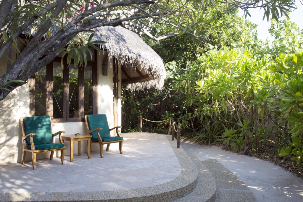 Terrasse der Sunset Beach Villa mit zwei Holzstühlen, Holzbeistelltisch und gemustertem Steinboden