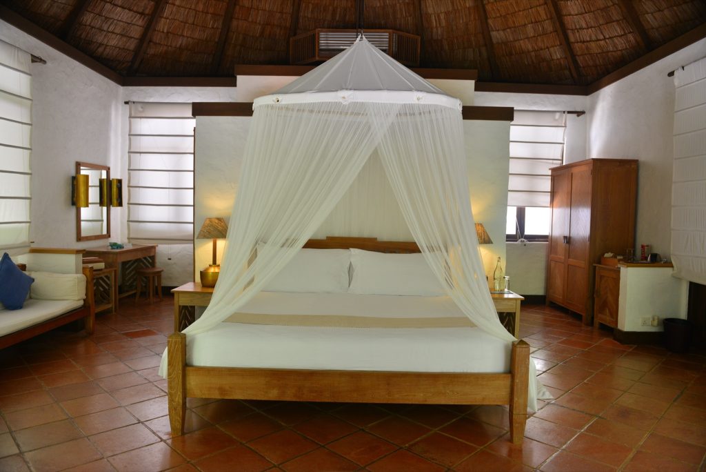 Großes Hotelzimmer der Sunset Beach Villa mit weißem Moskitonetz, hellem Holzmobiliar und Terrakottafliesen