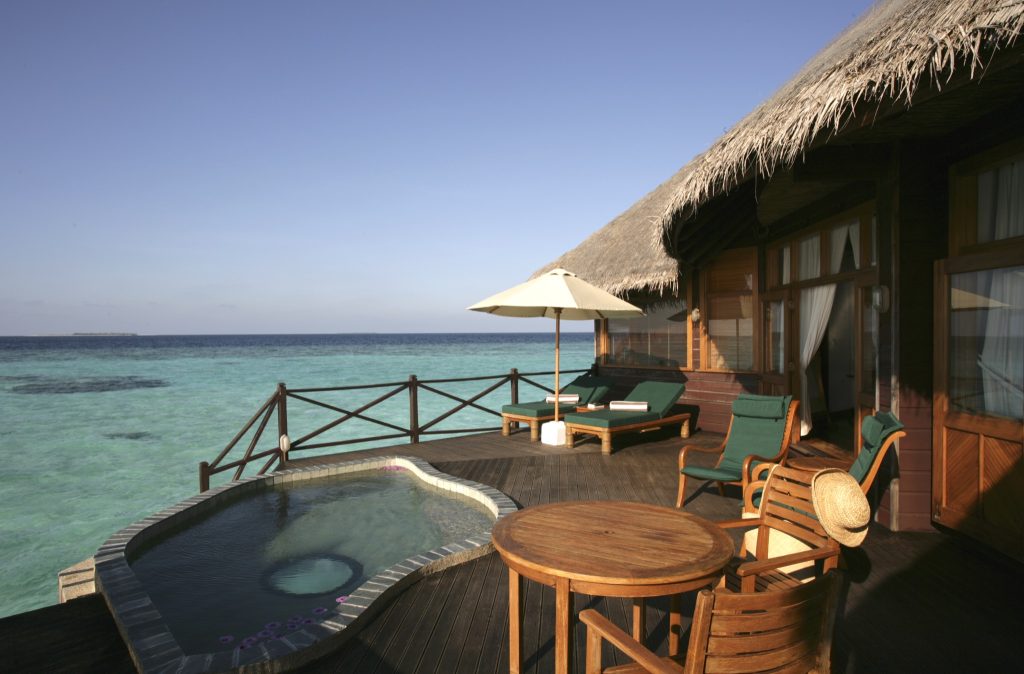 Terrasse der Sunset Lagoon Villa mit Holzfußboden, Holztisch, Liegestühlen, Sonnenschirm und kleinem Tauchbecken.