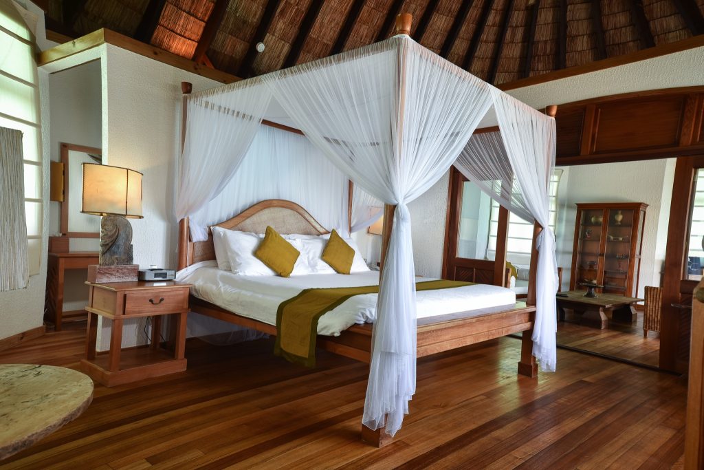 Zimmer der Sunset Lagoon Villa im Coco Palm Dhuni Kolhu mit Himmelbett, Holzboden und weißen Vorhängen