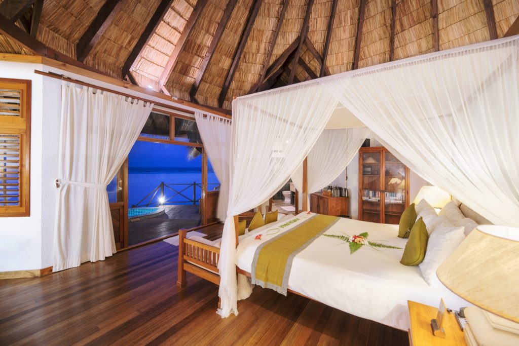 Geräumiges Zimmer der Sunset Lagoon Villa mit Baldachinbett, Holzboden und Blick aufs Meer auf den