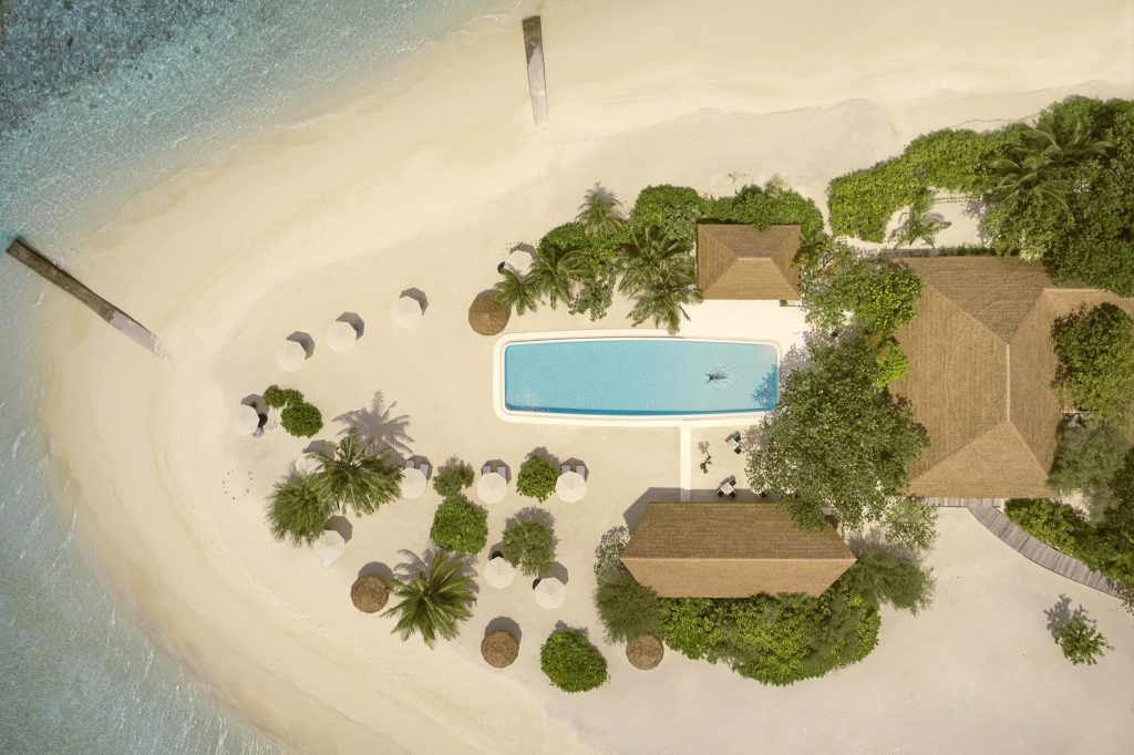 Rechteckiger Pool mit blauem Wasser, umgeben von grüner Vegetation und strohgedeckten Gebäuden auf den