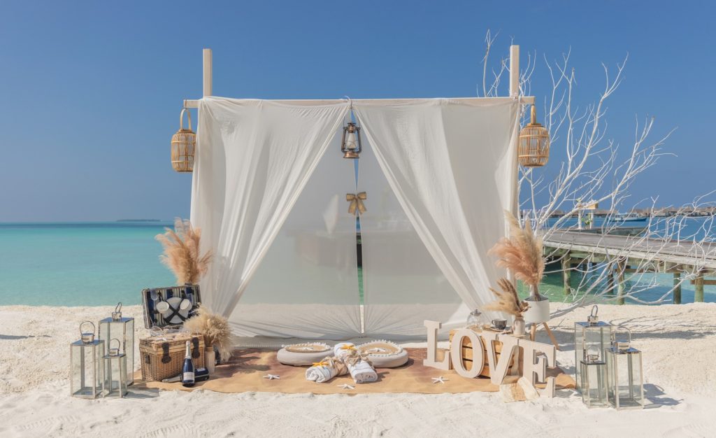 Strandarrangement mit weißer Leinwand, Teppich, LOVE-Buchstaben und Meer im Hintergrund auf den
