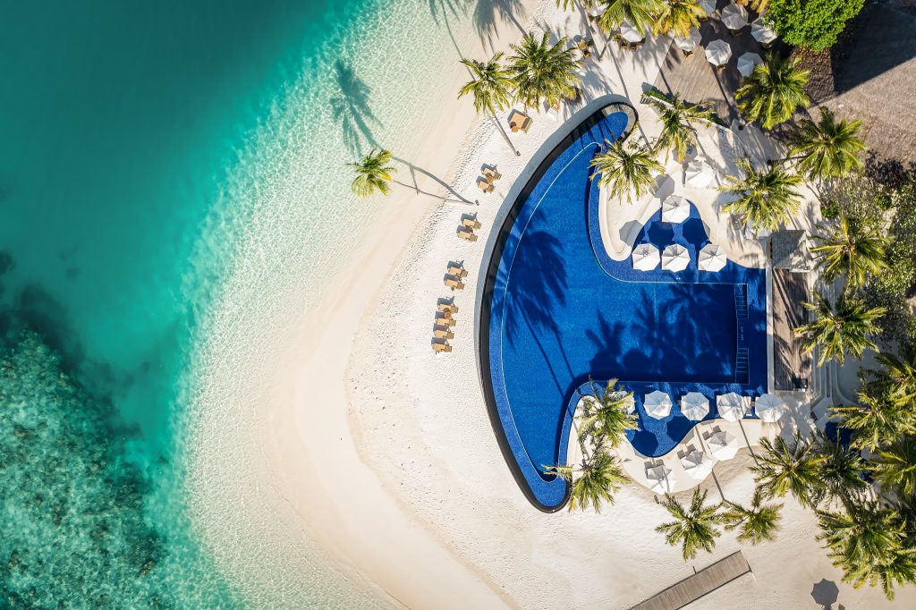 Luftaufnahme des Poolbereichs mit blauem Pool, weißen Sonnenschirmen und Palmen im Conrad Maldives Rangali Island