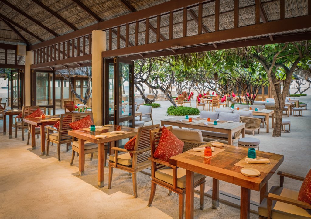 Offener Restaurantbereich im Atoll Market mit hellem Holzmobiliar, Sandboden und farbigen Kissen auf den
