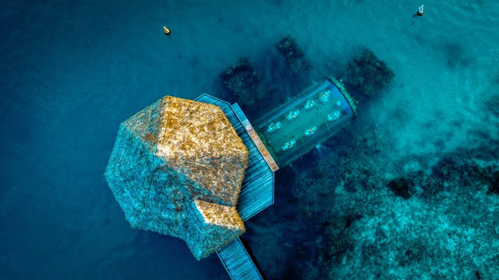 Vogelperspektive auf Restaurant Ithaa mit strohgedecktem Pavillon und Glas-Unterwassertunnel
