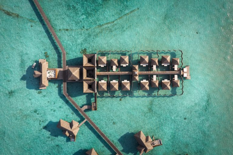 Luftaufnahme von Wasserbungalows auf Pfählen über türkisfarbenem Wasser im Conrad Maldives Rangali Island Wellness Spa.