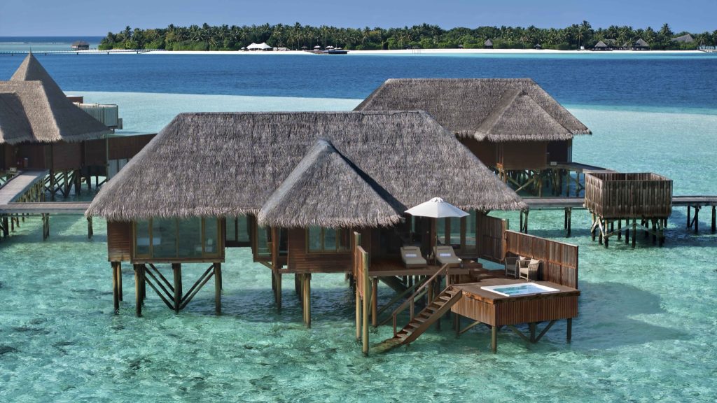 Wasserbungalows aus dunklem Holz mit Strohdächern über türkisfarbener Lagune bei Sonnenschein