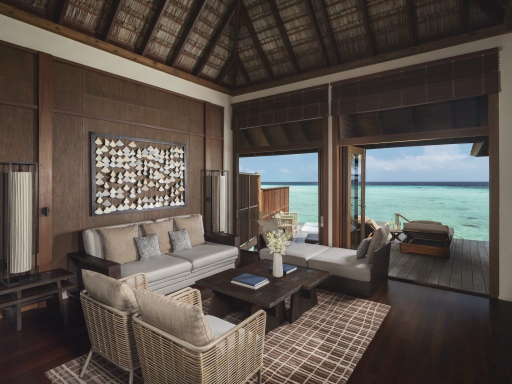 Wohnraum der Grand Water Villa im Conrad Maldives Rangali Island mit Holz- und Rattanmöbeln und Meerblick