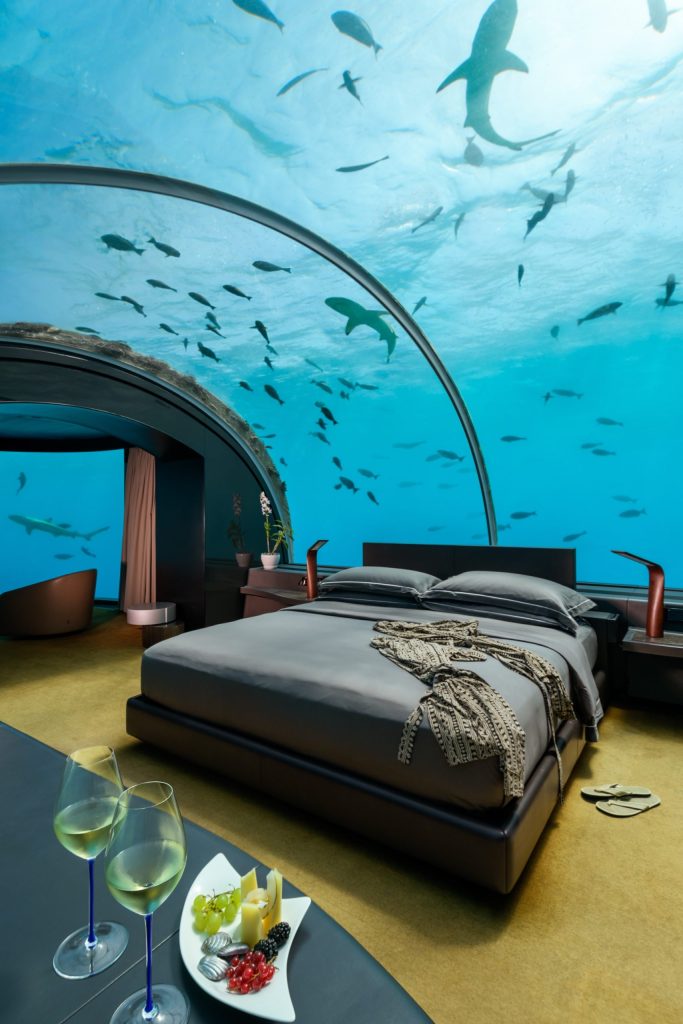 Unterwasserzimmer Muraka mit gewölbter Glasdecke, Blick auf Fische und Hai, Bett und Tisch mit Snacks