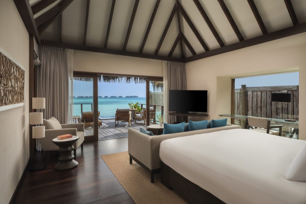 Zimmer der Sunrise Water Villa mit Doppelbett, Sofa, Holzboden und Meerblick auf den