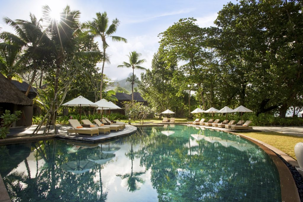 Poolbereich im Constance Ephelia Hotel auf den Seychellen mit weißen Sonnenschirmen, Holzliegen und tropischer Vegetation