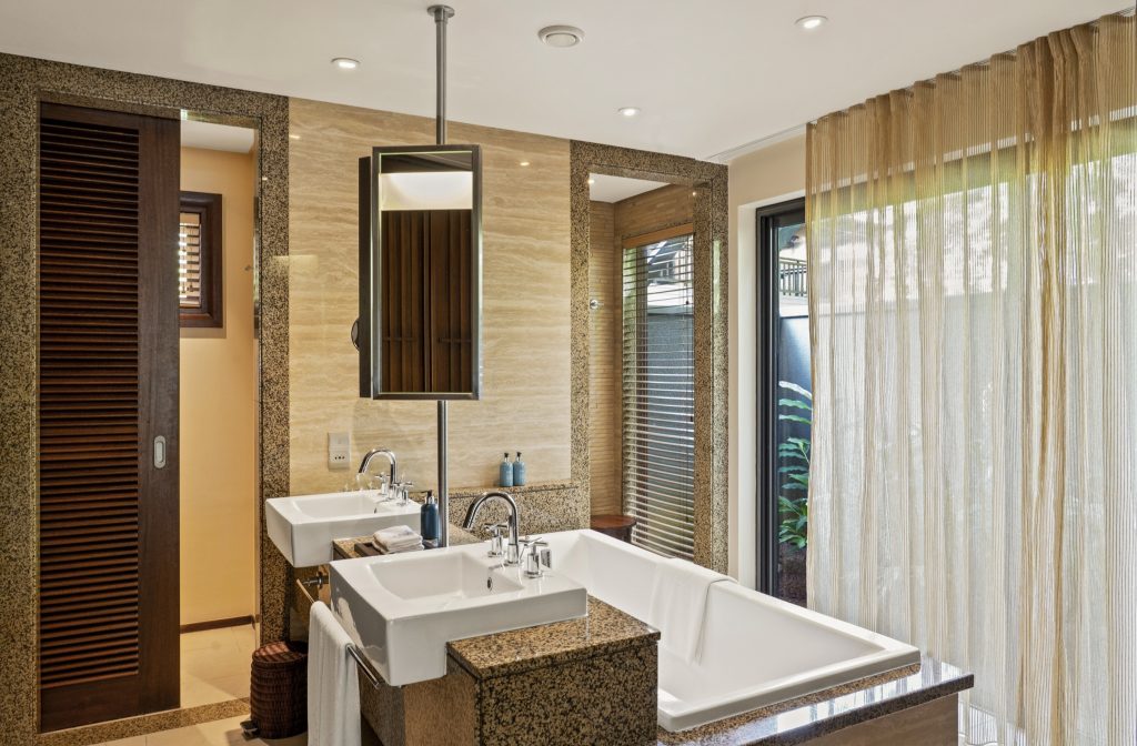 Badezimmer der Junior Suite im Constance Ephelia mit Badewanne, zwei Waschbecken, Granitboden und Holzfenstern