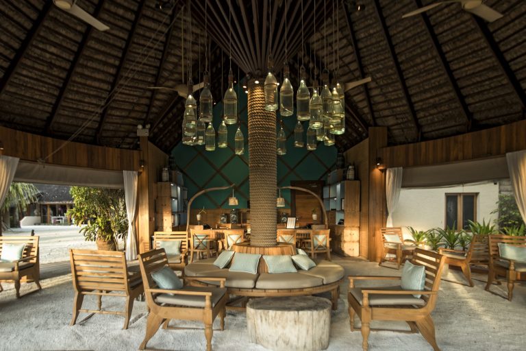 Offene Lobby im Constance Moofushi mit Holzsäule und kreisförmig angeordneten Glasflaschenleuchten